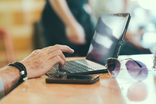 Auf dem Bild ist ein Laptop, ein Handy und eine Sonnenbrille zu sehen. 