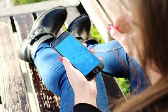 Auf dem Bild ist ein Mädchen mit einem Handy in der Hand zu sehen.